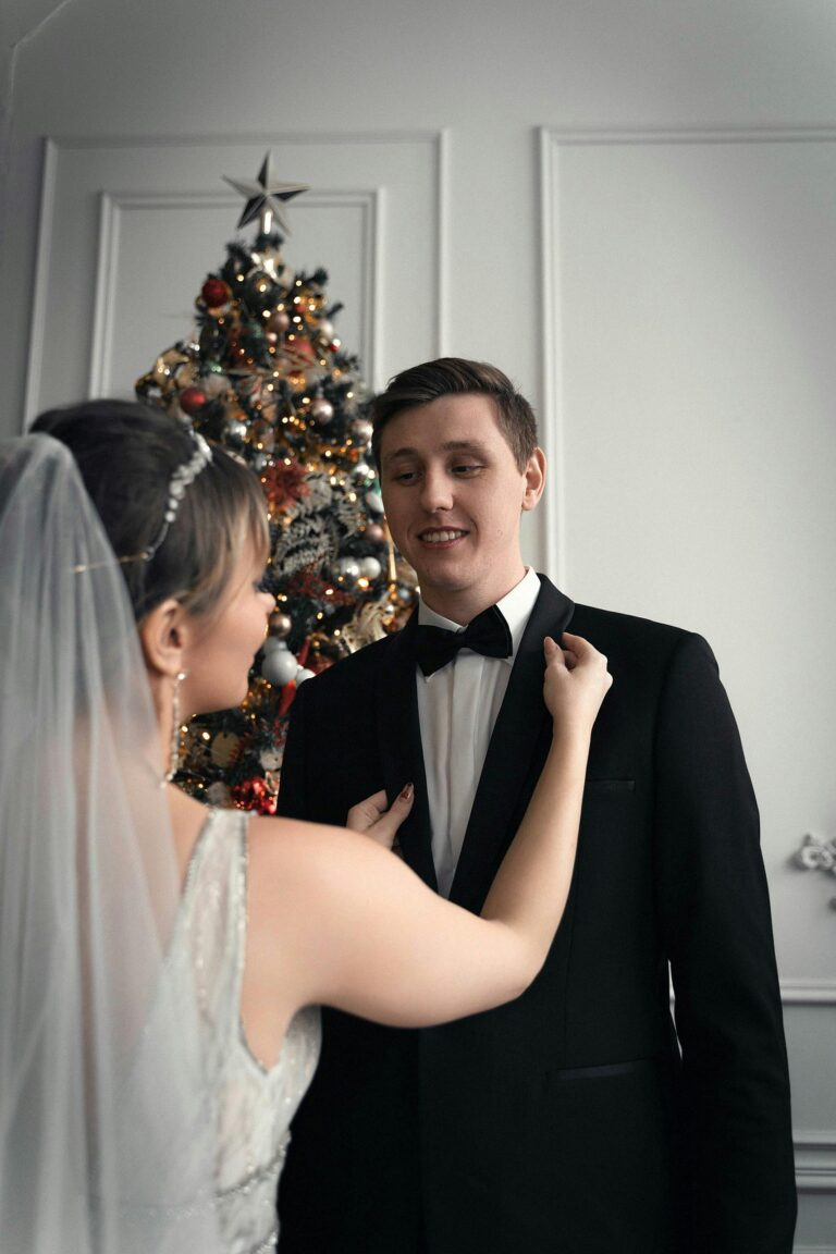 Bride and groom smiling indoors by a decorated Christmas tree, embracing festive wedding moments.