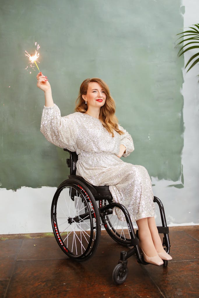 Glamorous woman in wheelchair holding a sparkler, celebrating indoors.